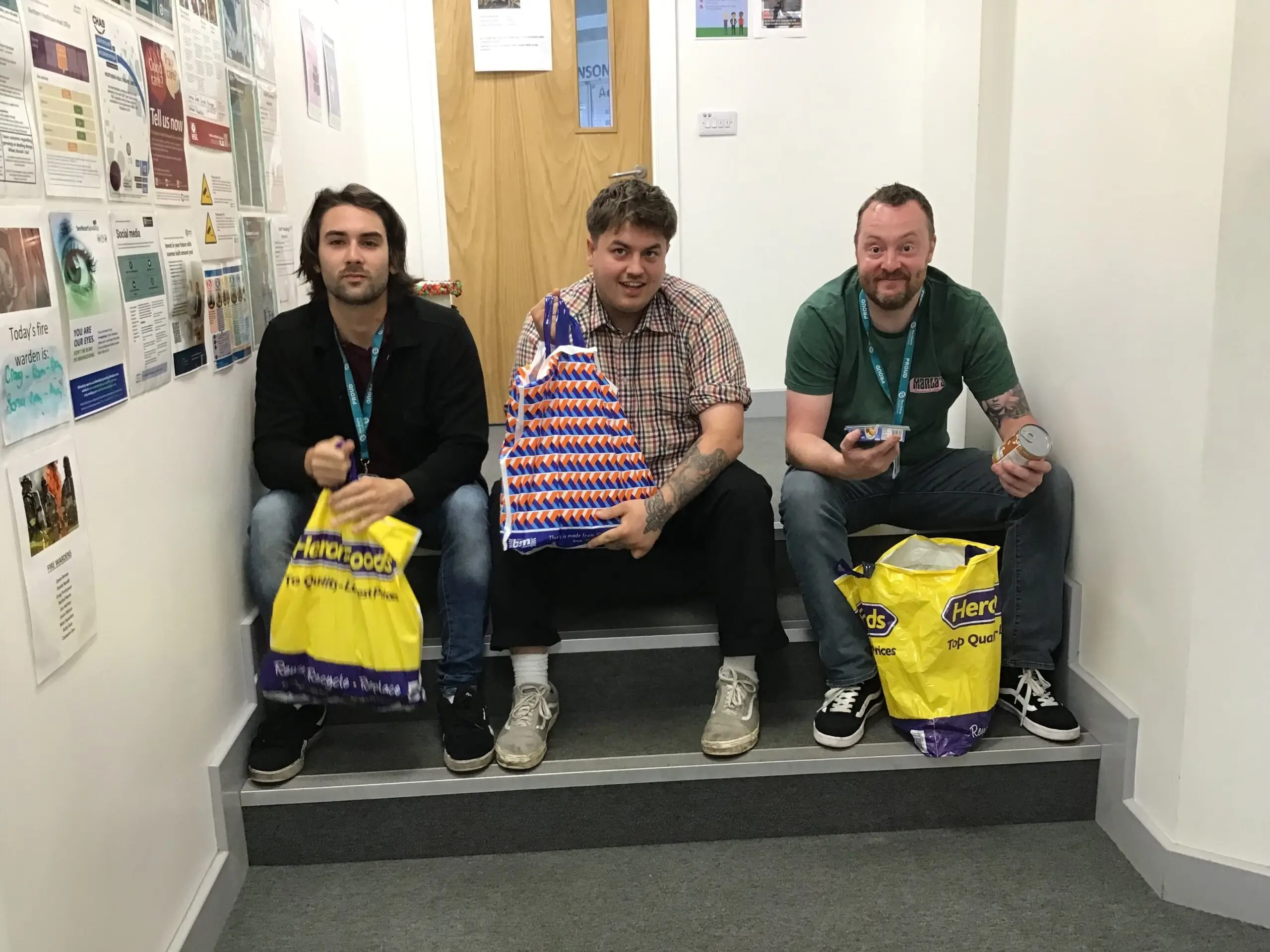 3 team members sitting on stairs holding bags of food