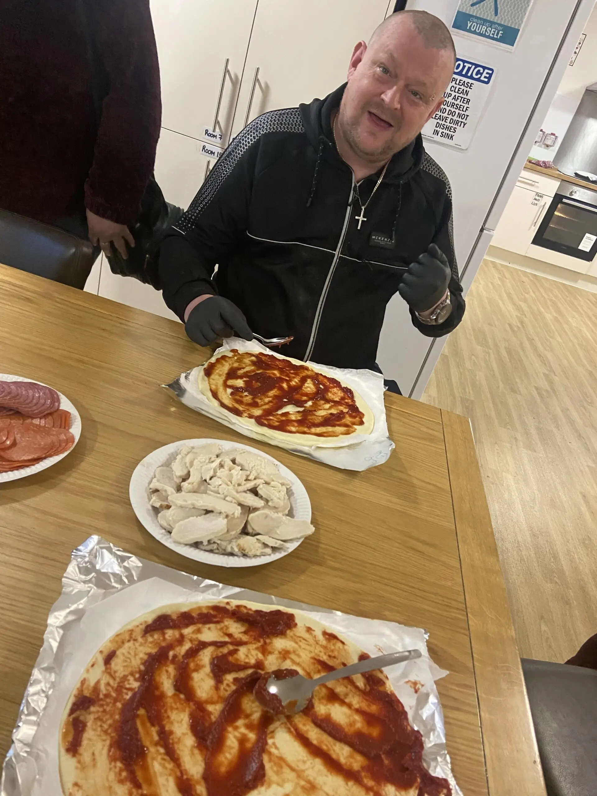 man adding pizza sauce to base