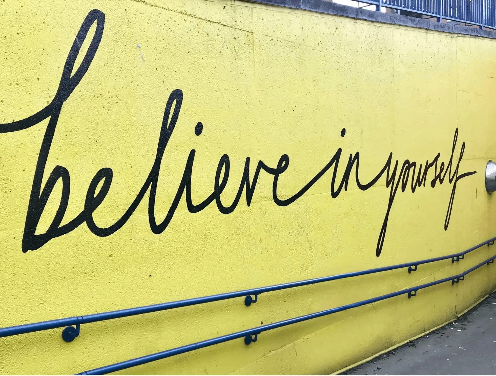 Yellow wall with graffiti saying 'believe in yourself' for a blog about the benefits of self-affirmations for mental health.