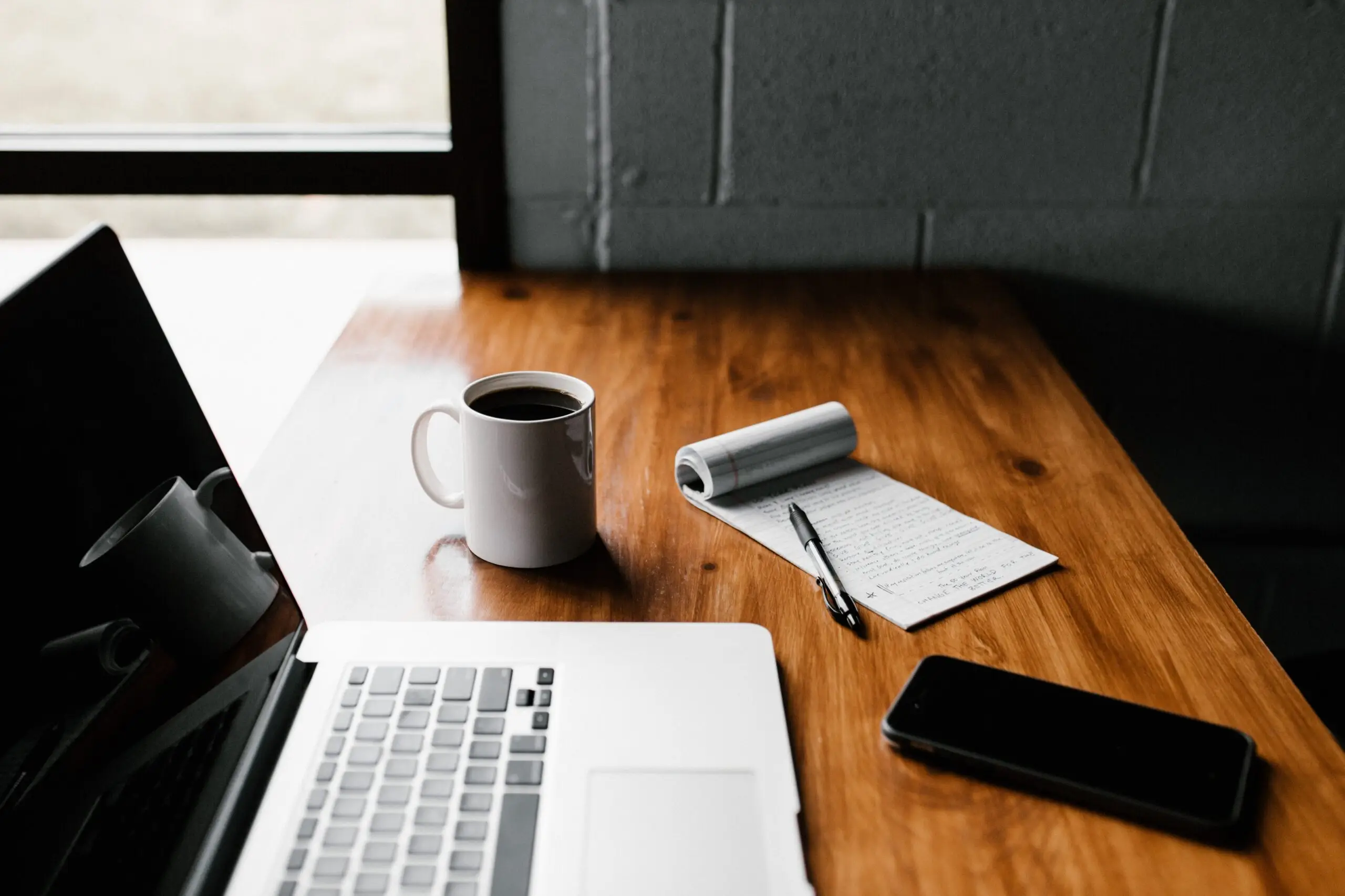 wooden desk with laptop, notepad and coffee cup on top