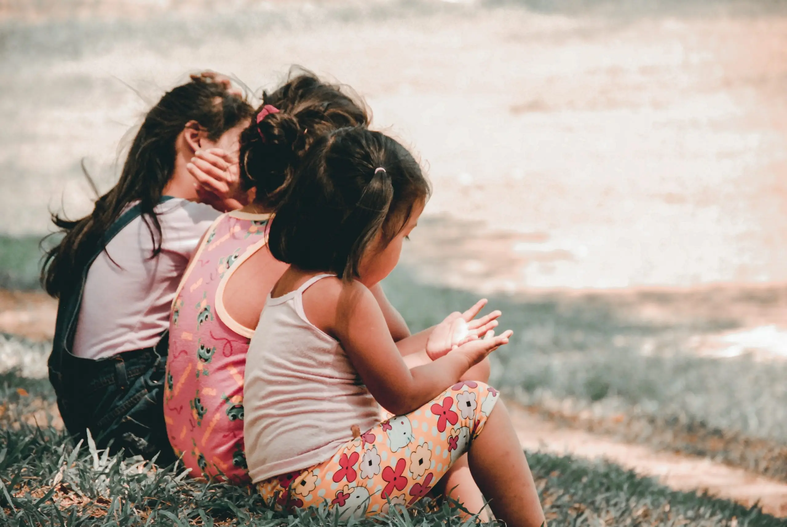 3 young girls sitting side by side on grass