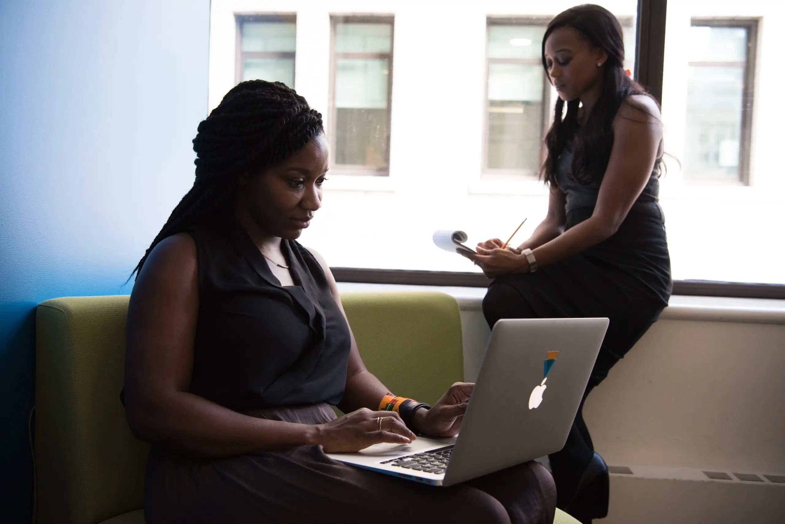 woman working on laptop and woman writing in notepad