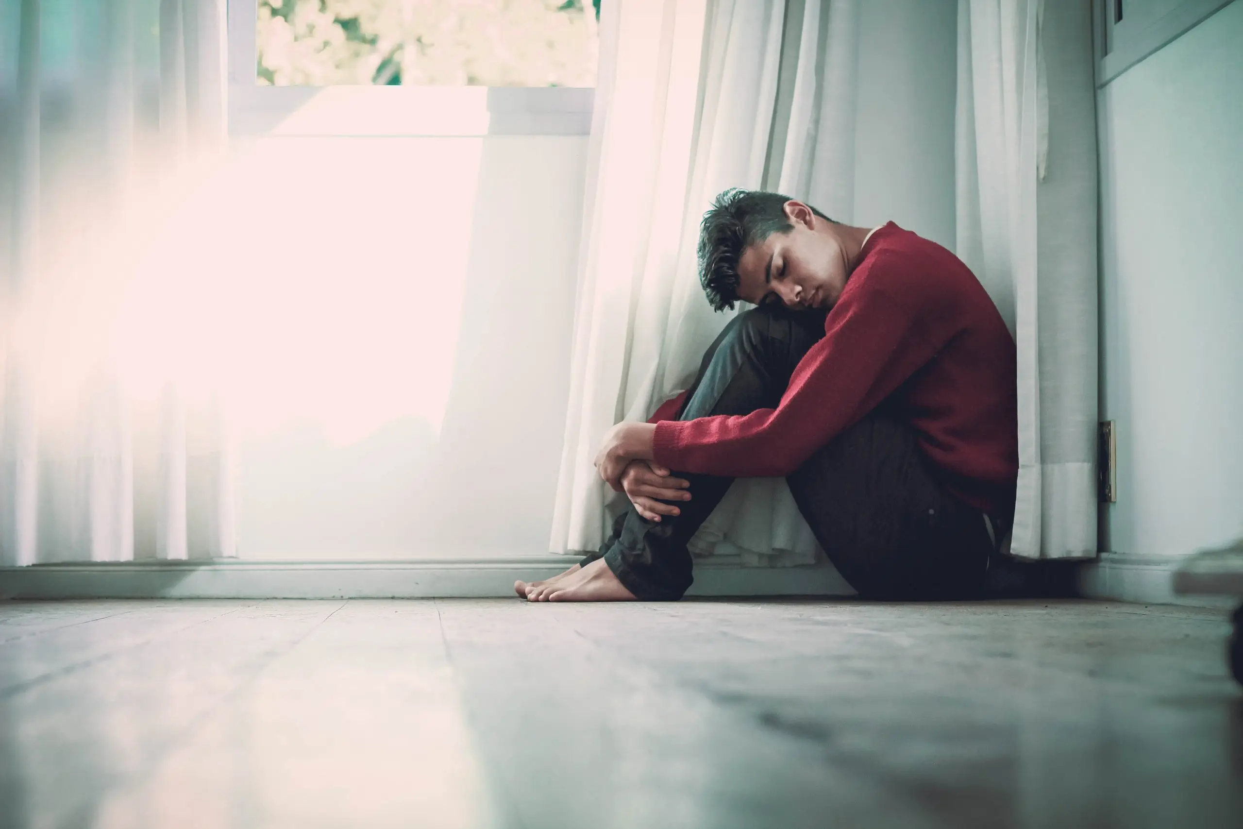 man sitting on floor with legs tucked up and head resting on knees
