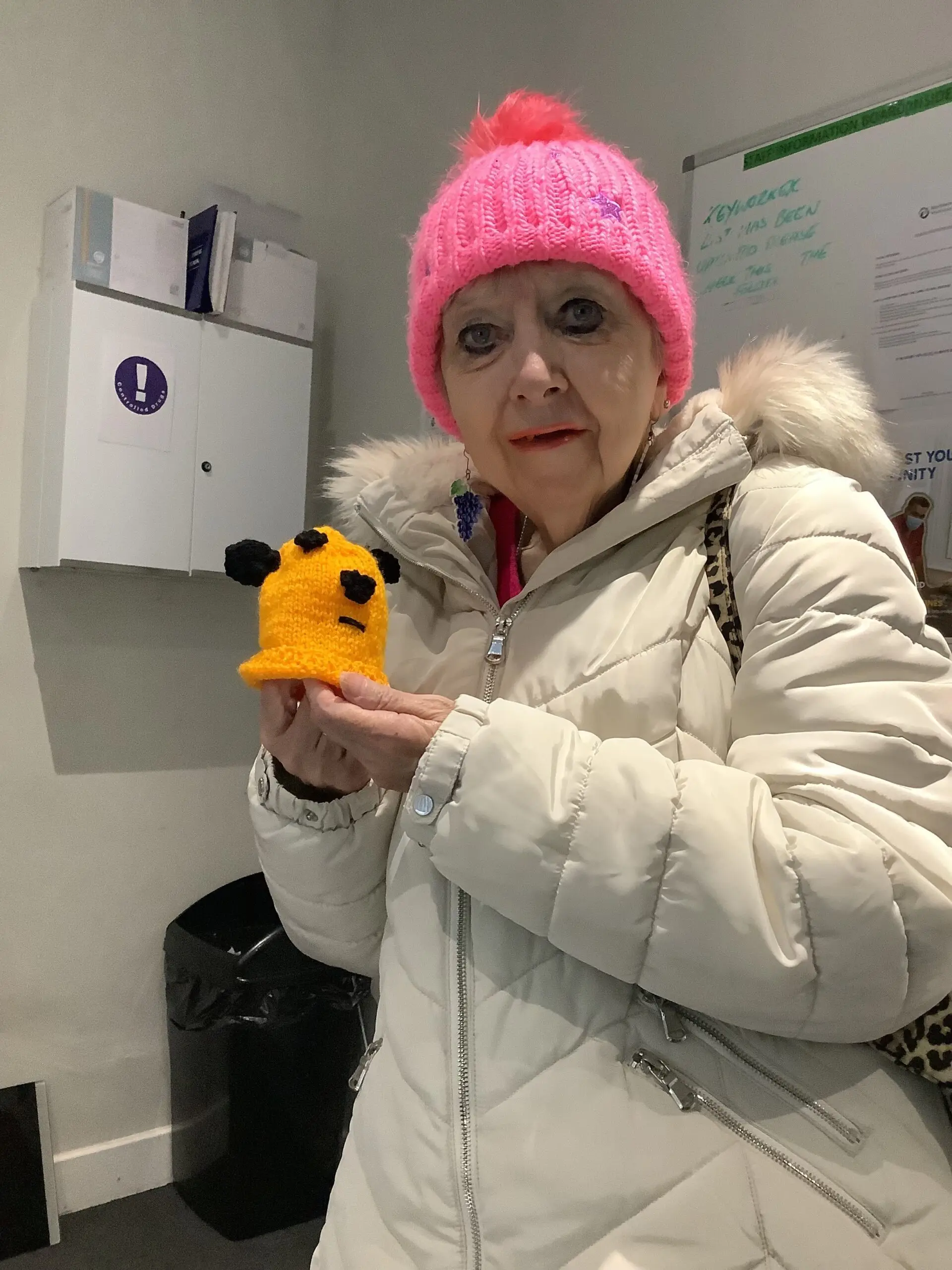 resident in pink woolly hat and white coat holding yellow knitting