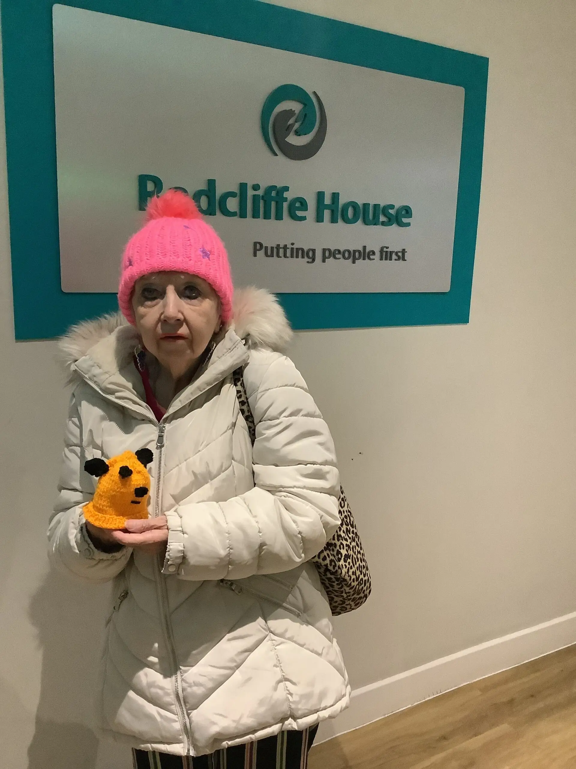 resident in pink woolly hat and white coat holding yellow knitting