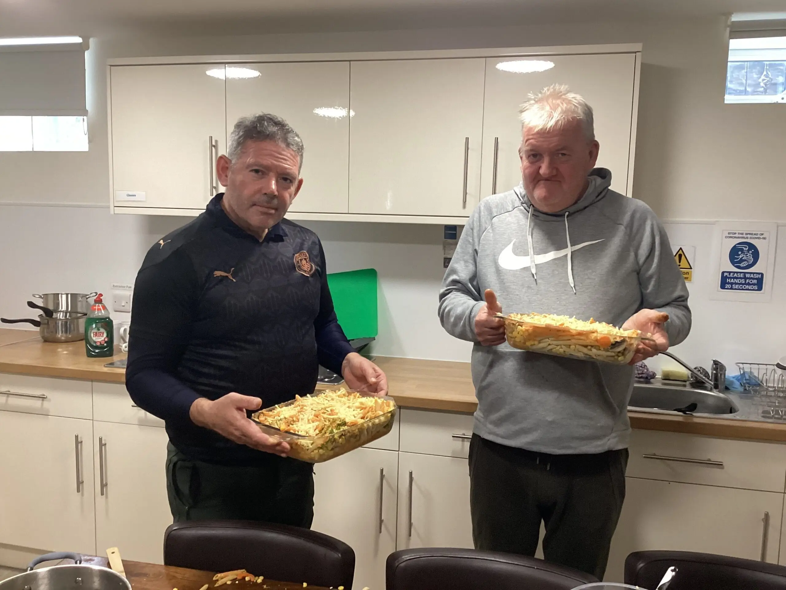 2 male residents holding dishes of homemade pasta