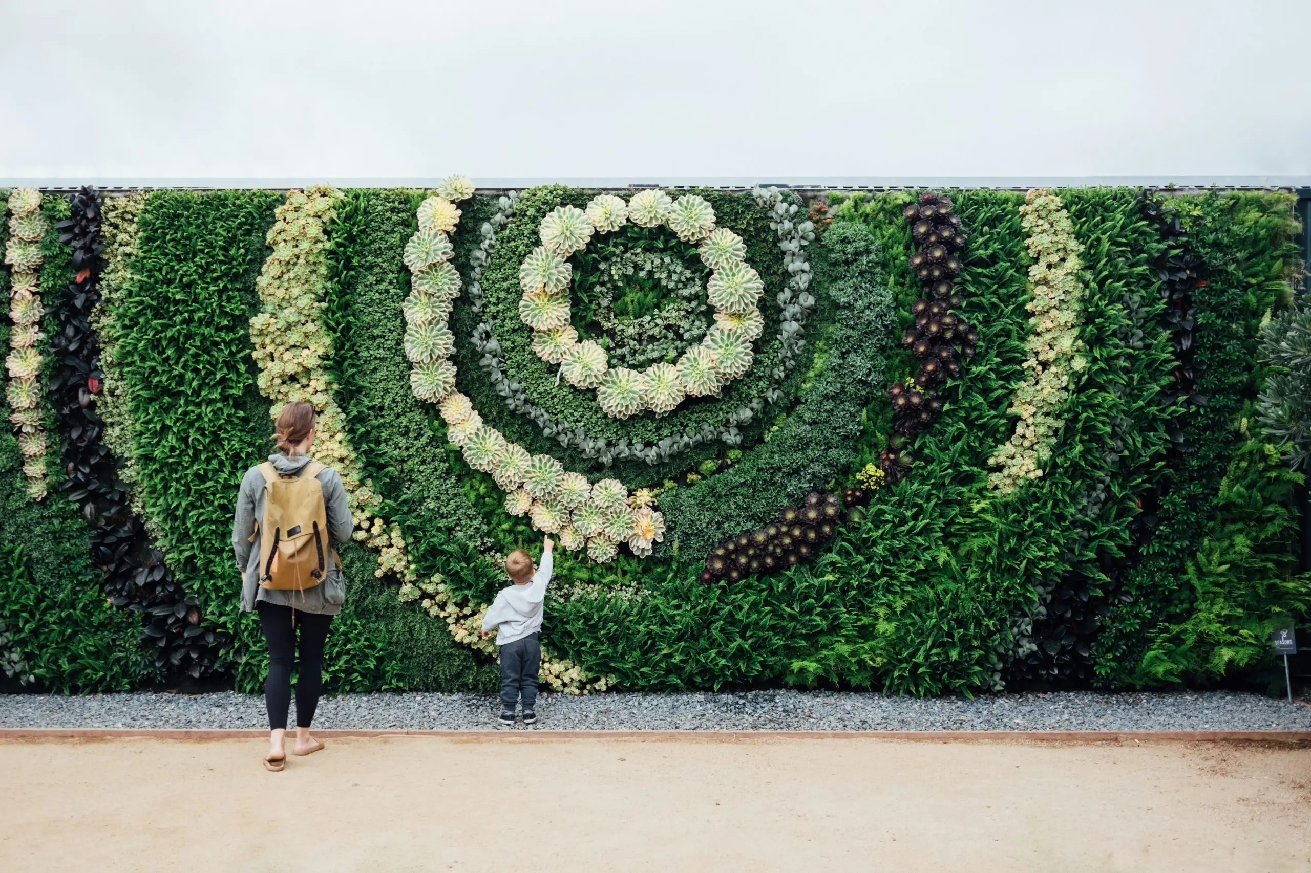 A mother caring for, and watching over, her young child as they explore a modern garden, highlighting the mental health of parents today.